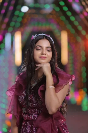 Bride in a ruffled maroon outfit with eyes closed posing against a blurred bokeh light background